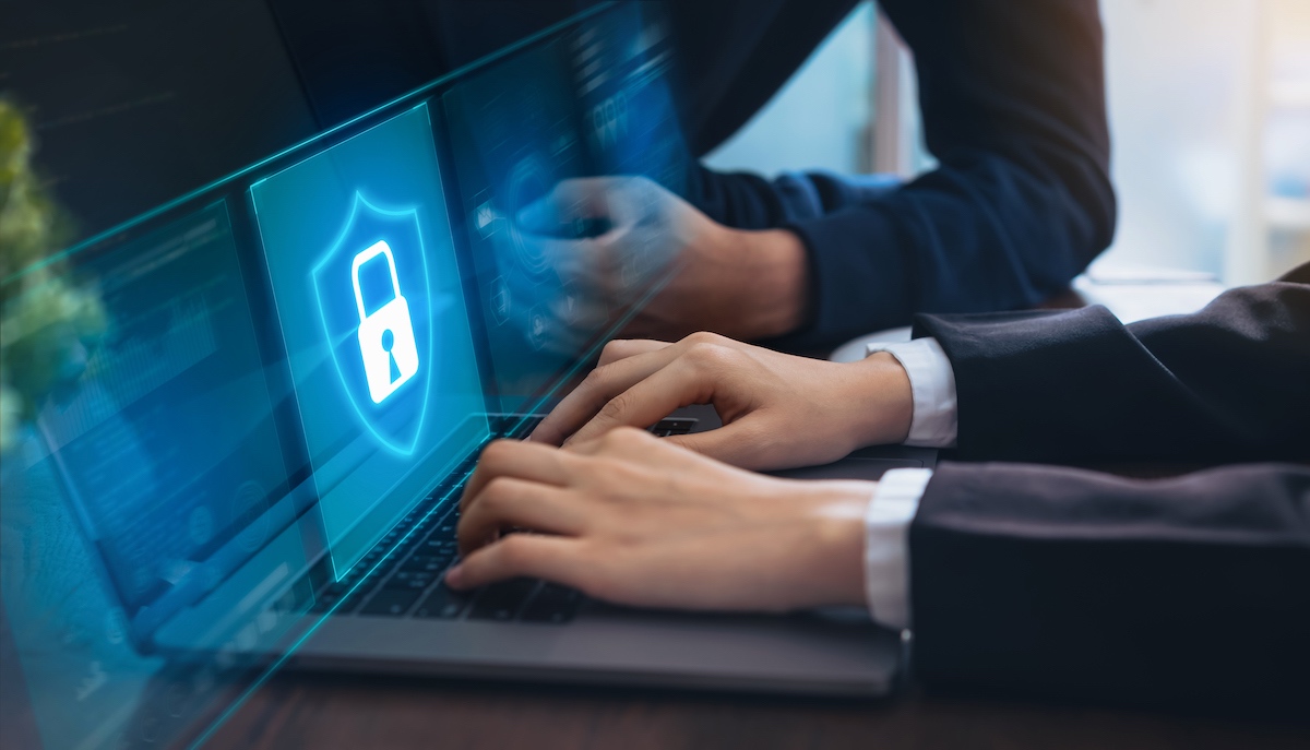 Business Man’s Hands Typing On A Laptop With A Blue Cyber Security Screen With A Large White Shield And A Padlock On It