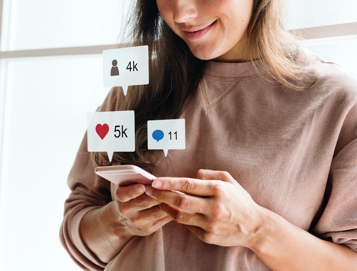 Woman Holding And Looking At Her Mobile Phone While Social Media Icons Float Above It
