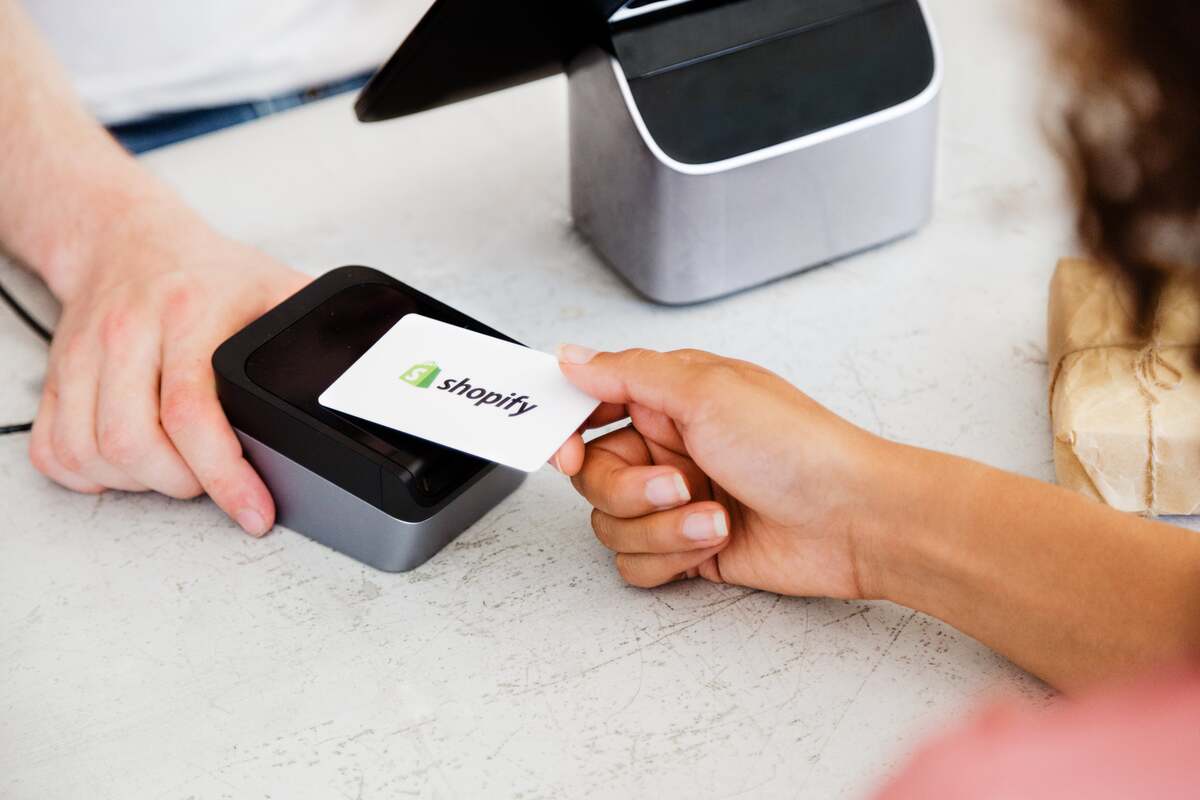 Hand tapping a Shopify-branded credit card onto a card reader for payment.