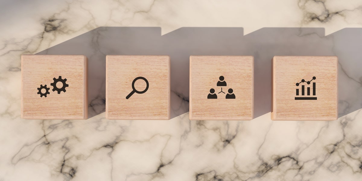 Wooden blocks on marble surface showing SEO process icons: settings, search, team, and analytics