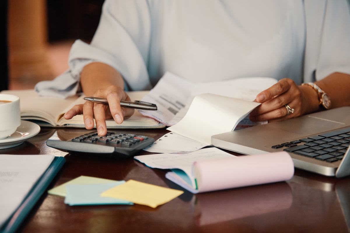 hands typing on a calculator and writing notes on a desk