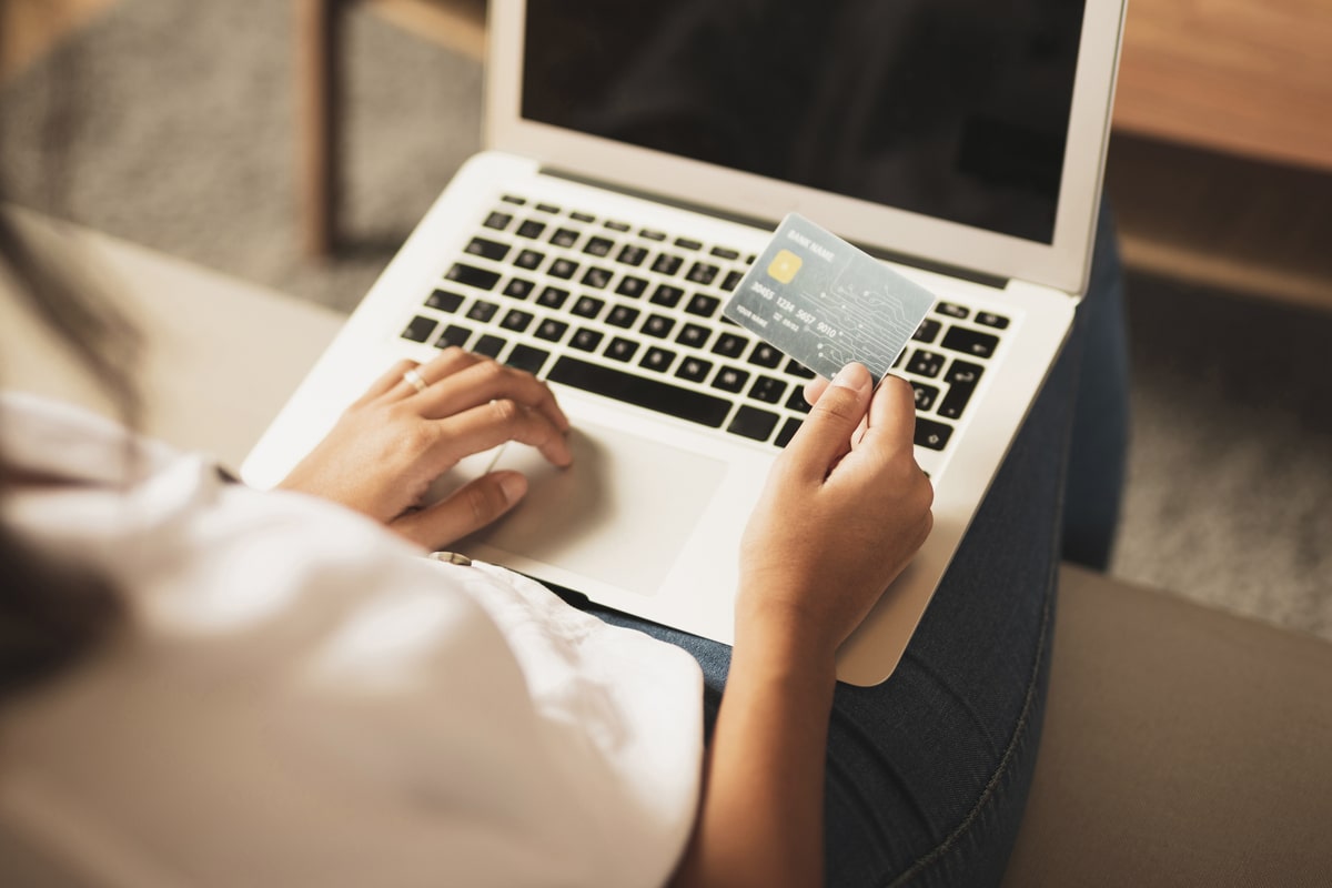 hands holding a credit card in front of a laptop