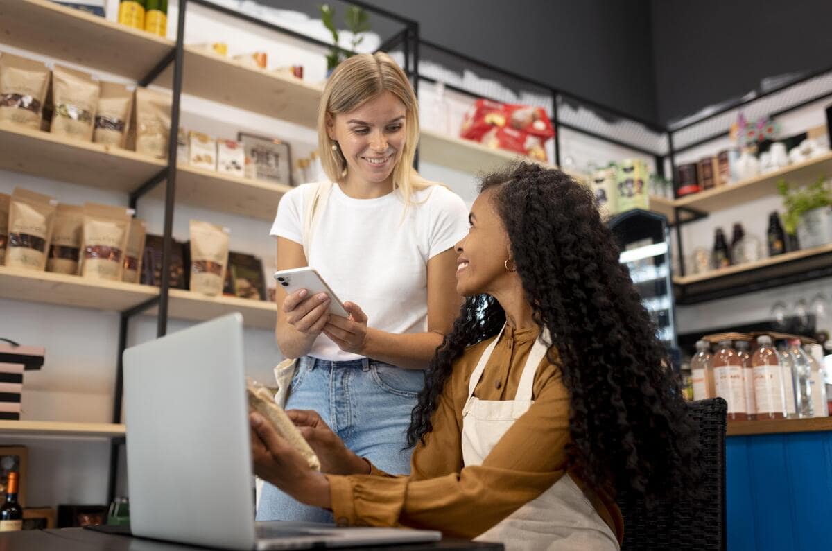 two woman working on laptops in a small business setting and talking