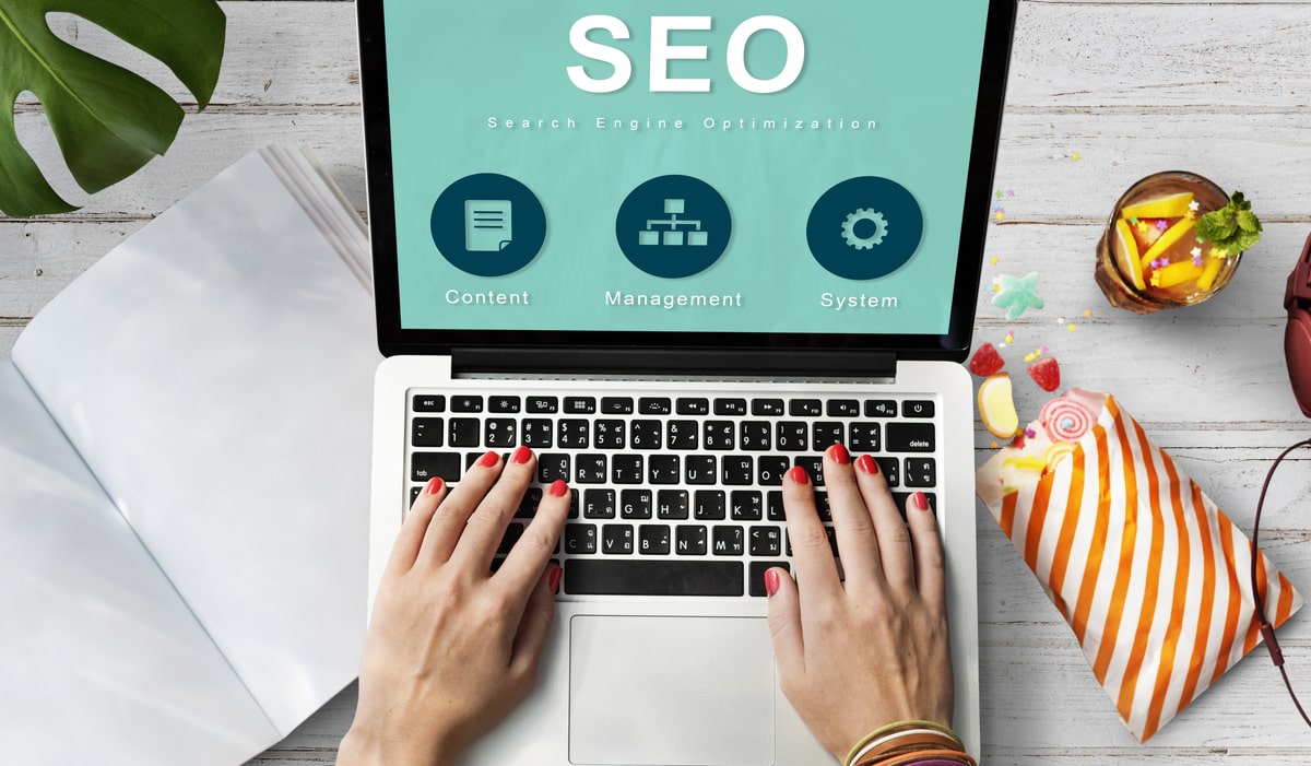 Hands typing on laptop with SEO dashboard showing content, management, and system icons