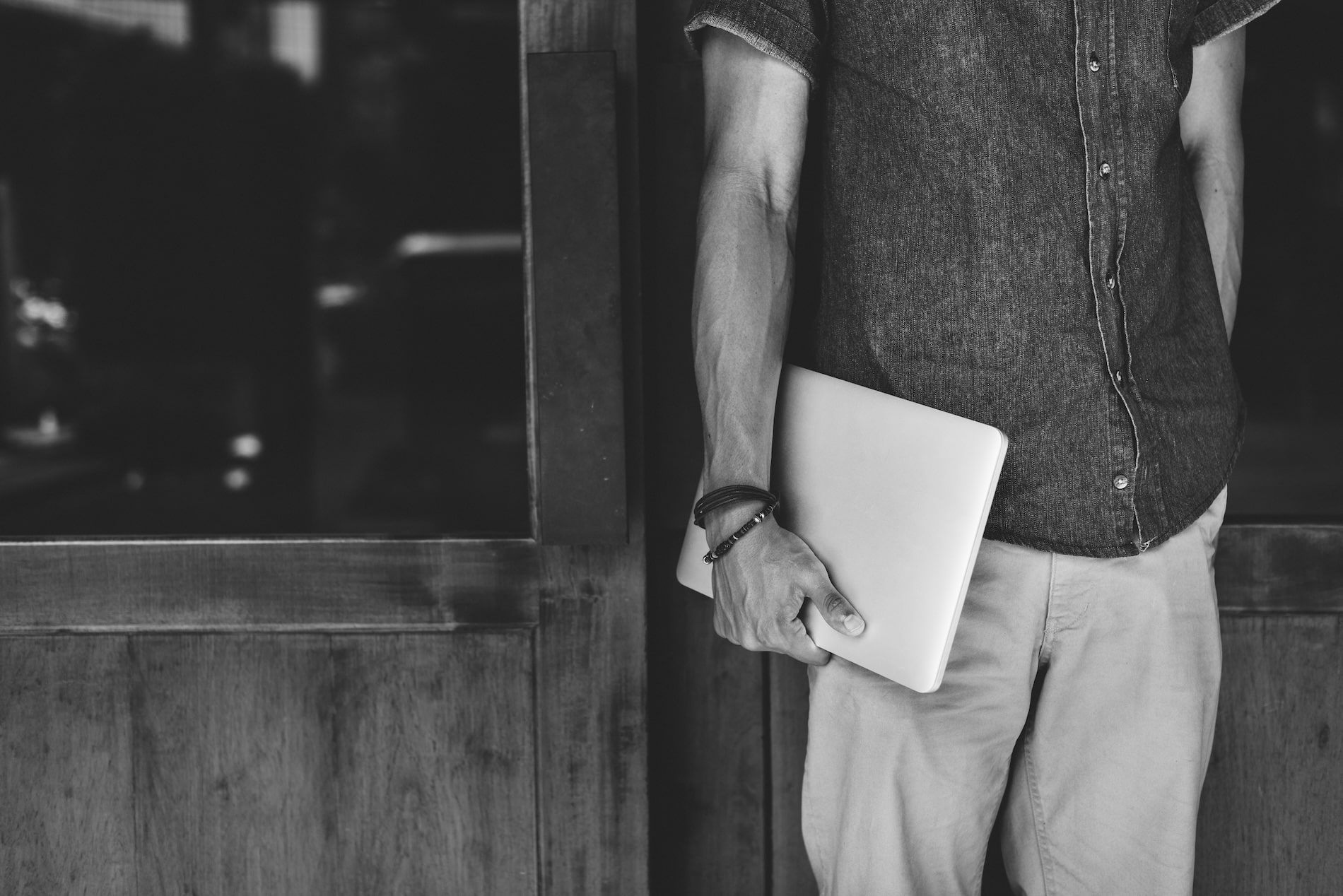 Man standing by a door holding a closed laptop representing a modern business owner